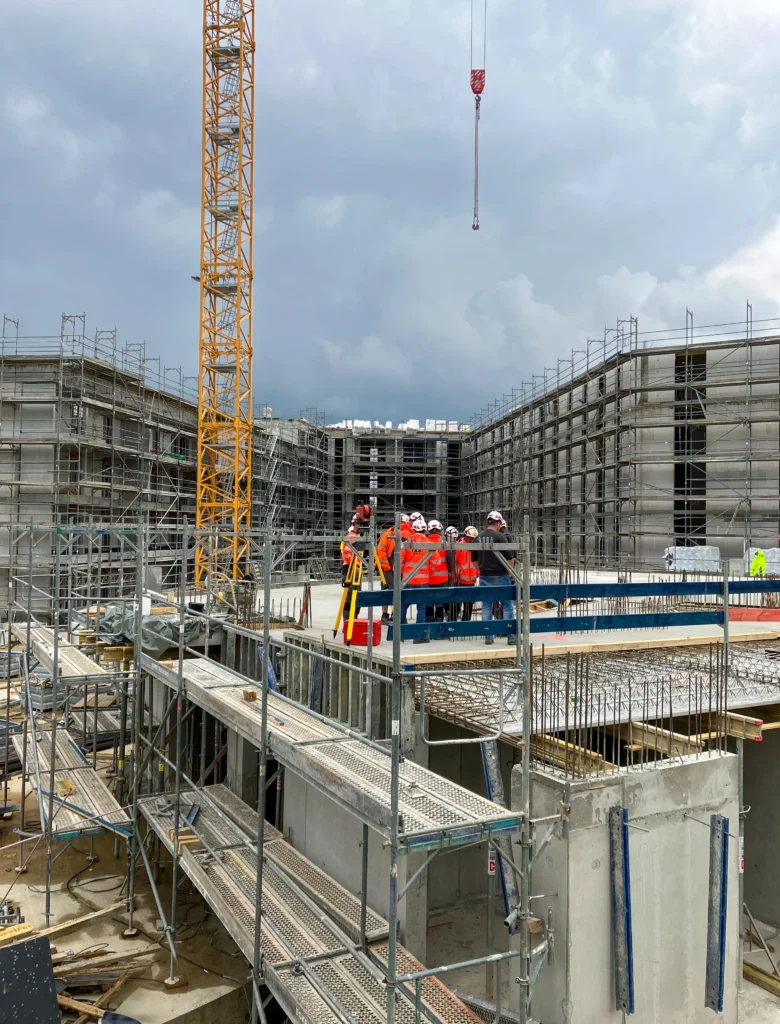 Gruppe von Mitarbeitern auf einer Baustelle, Bauwerk Rohbau im Hintergrund, Kran auf der linken Seite