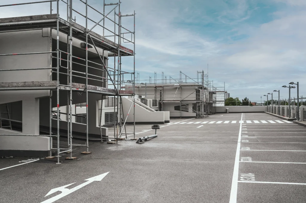 oberstes Parkdeck eines Parkhauses, Außenaufnahme, Gebäude teilweise noch im Gerüst, im Hintergrund blauer Himmel, Parkplätze leer