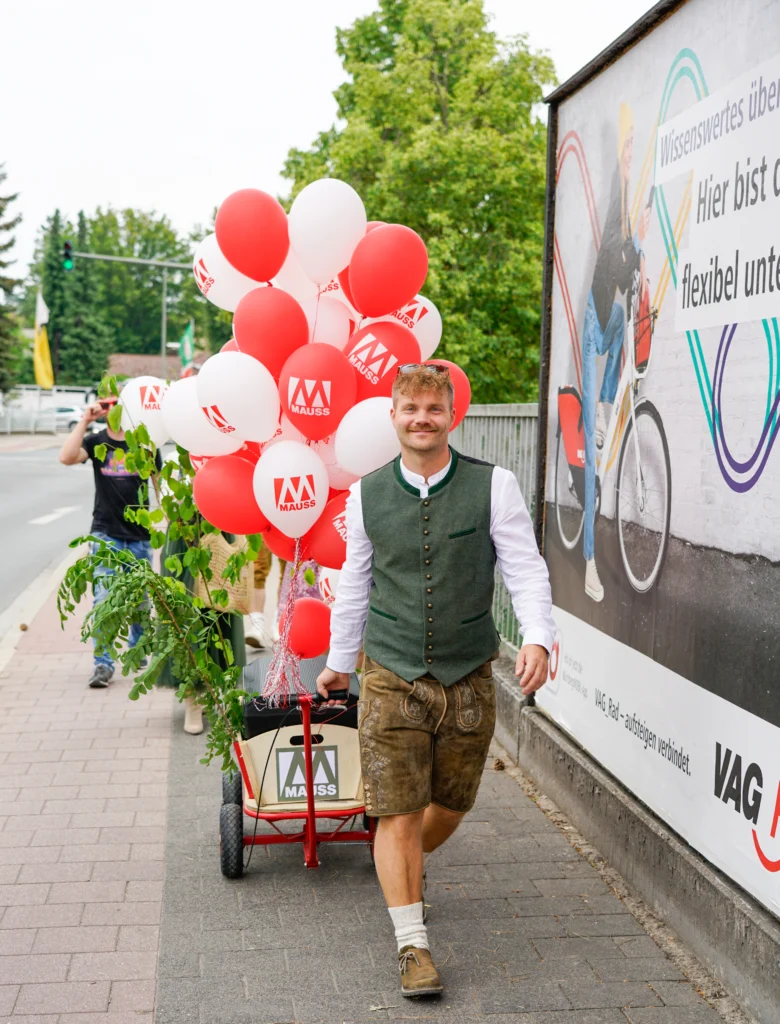 Mann in Tracht zieht einen Bollerwagen , an dem Luftballons befestigt sind