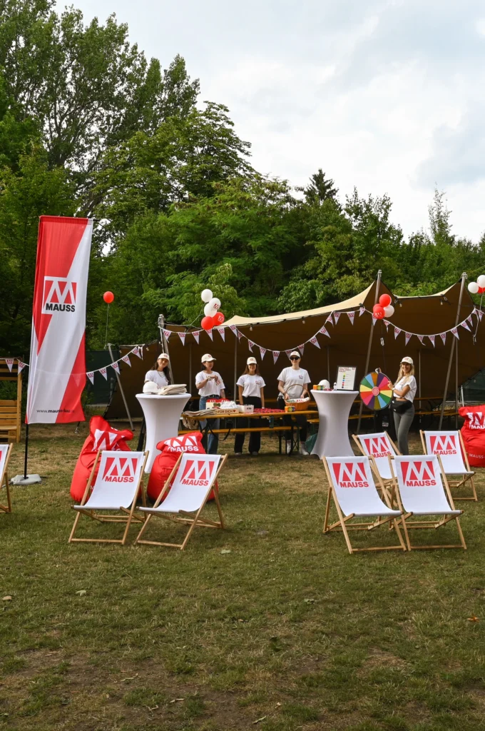 MAUSS-Stand auf der Wöhrmühle 2025, im Vordergrund Beachstühle und Sessel mit MAUSS-Logo, im Hintergrund ein Tisch inkl. Glücksrad, MAUSS-Mitarbeitenden im Hintergrund, schauen in die Kamera
