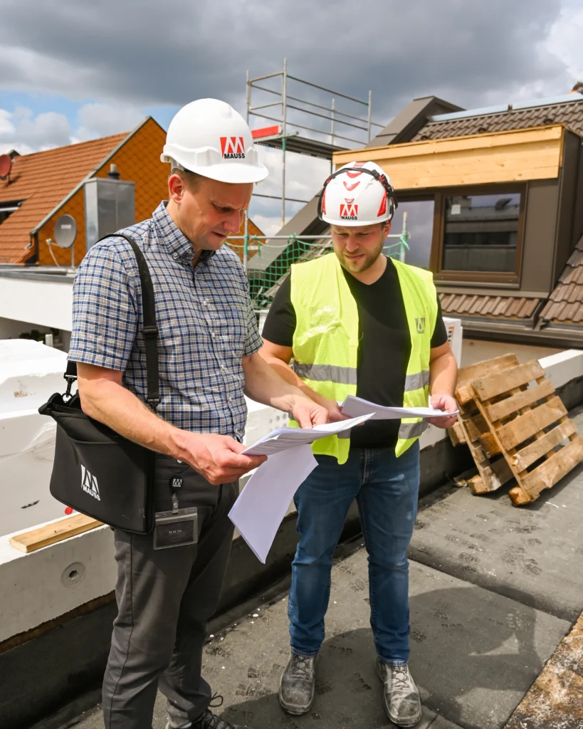 Zwei Mitarbeiter von MAUSS BAU überprüfen Pläne auf einer Baustelle