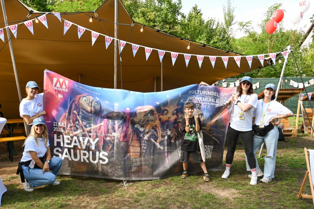 Junge macht "Pommes-Gabeln" mit den Händen, vor einem Heavysaurus-Banner, gehalten von den Marketing-MÄUSSEN
