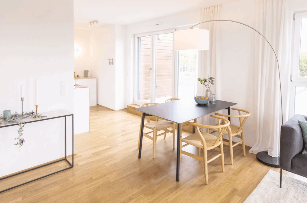 Moderner Essbereich mit schwarzem rechteckigem Tisch, vier Holzstühlen, großem Bogenlampenständer und hellen Vorhängen vor bodentiefen Fenstern.