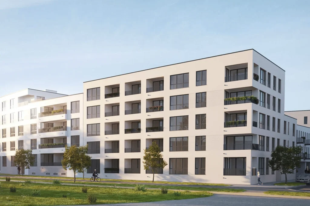 Das Bild zeigt mehrere moderne, mehrgeschossige Wohngebäude mit hellen Fassaden und großen, gleichmäßig angeordneten Fenstern. Die Gebäude verfügen über Balkone und Loggien, davor liegen Grünflächen mit Bäumen sowie ein Geh‑ und Radweg. Die Architektur wirkt klar, modern und offen gestaltet.