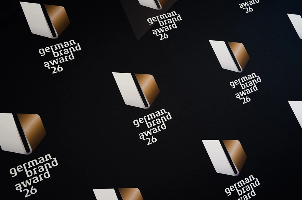 Muster aus mehrfach wiederholtem Logo des German Brand Award 26 mit stilisiertem gold-weiß-schwarzem Symbol auf schwarzem Hintergrund.