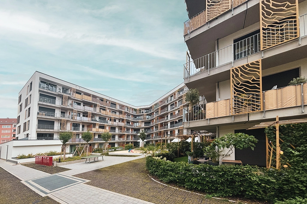 Moderner Wohnkomplex mit mehreren mehrstöckigen Gebäuden, Balkonen und begrüntem Innenhof unter bewölktem Himmel.